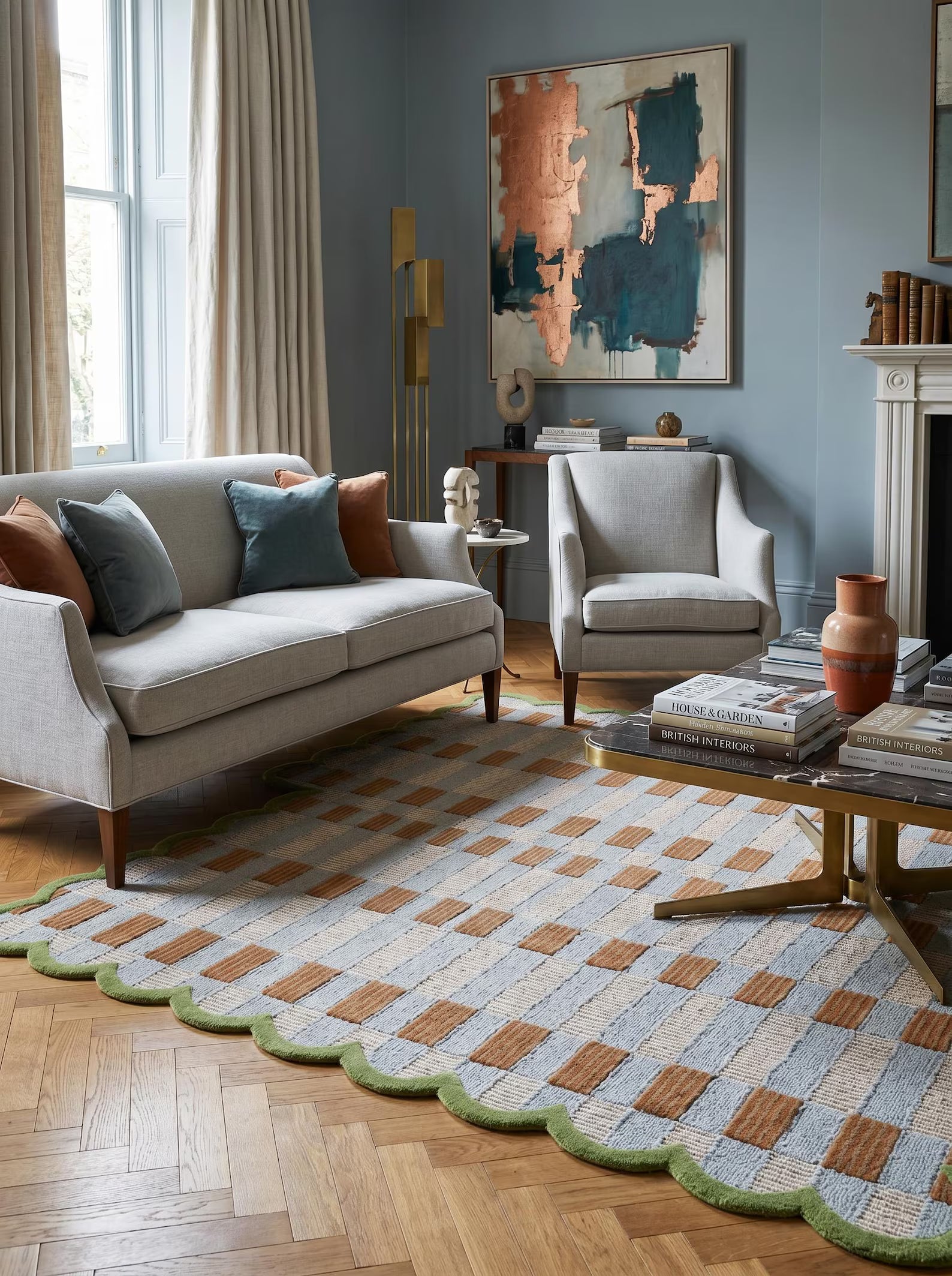 A styled living room featuring a large patterned area rug with a scalloped green edge, styled with a light gray sofa, armchair, and wooden herringbone floor.