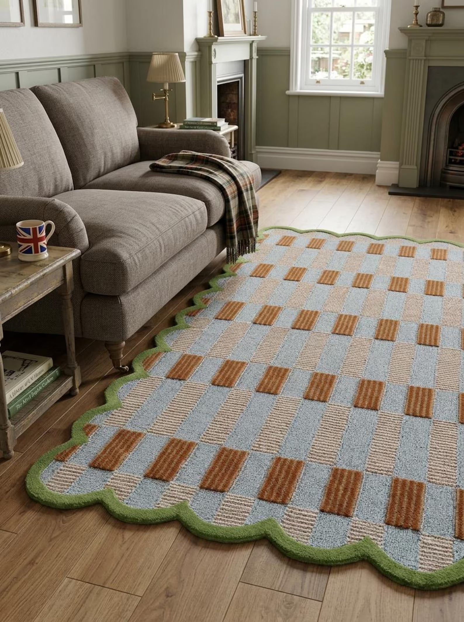 A rectangular area rug with a scalloped edge, featuring a woven checkerboard pattern in light blue, beige, and brown, styled on a wooden floor in a living room next to a gray sofa.