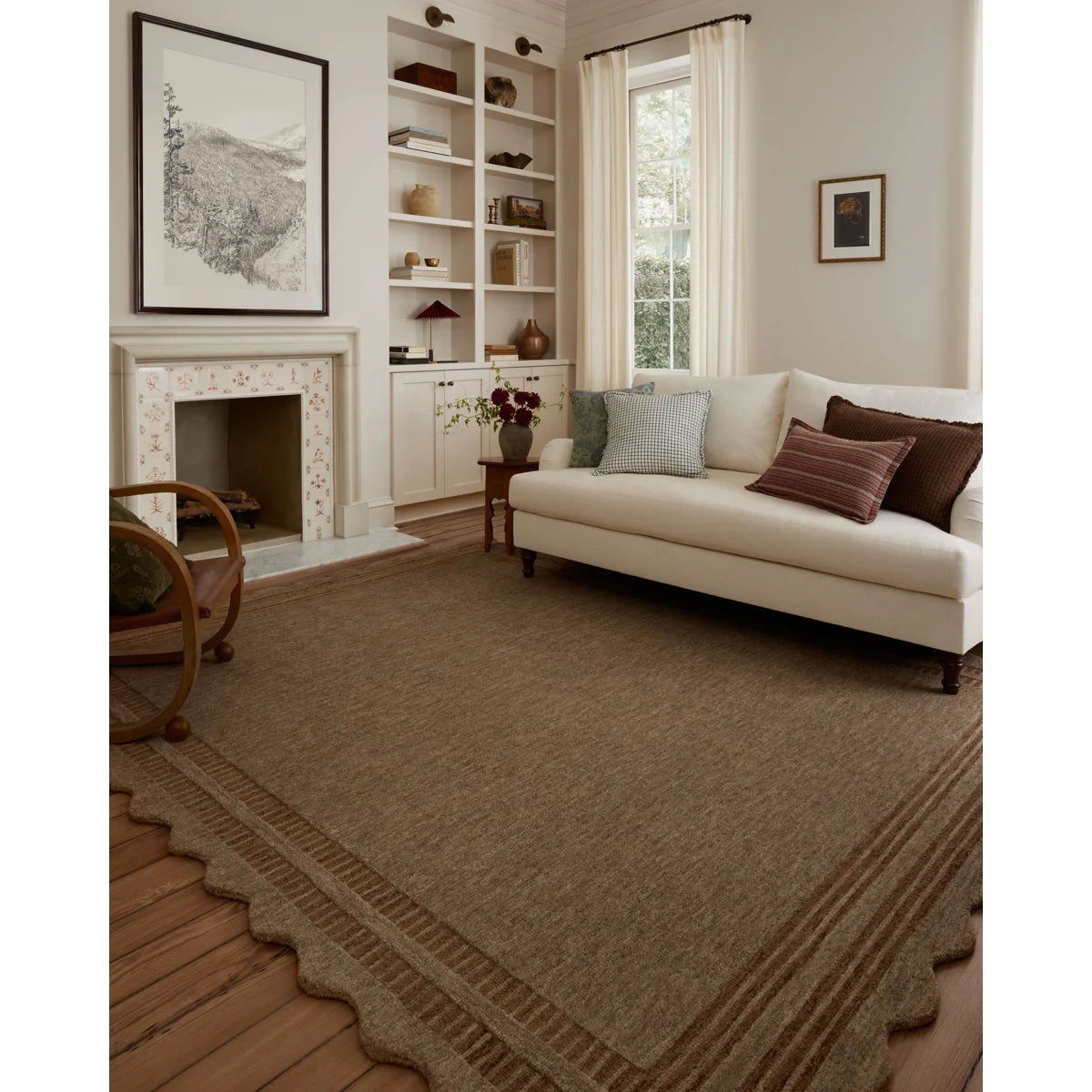 A large brown area rug with a scalloped edge and subtle striped pattern, shown in a styled living room with a cream sofa, fireplace, and built-in shelves.