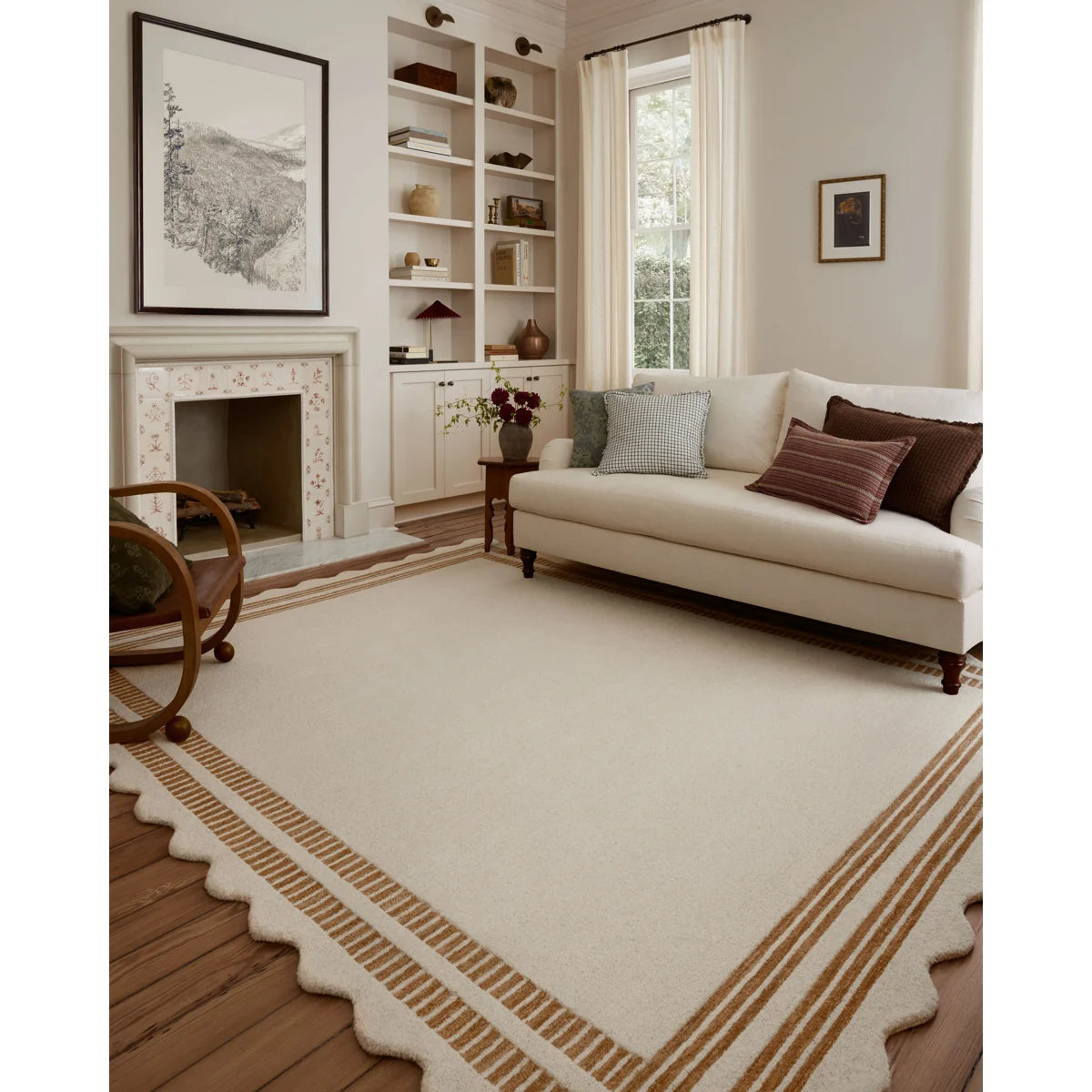 A large cream-colored area rug with a scalloped border and tan stripe accents, styled in a bright, modern living room with a cream sofa, fireplace, and built-in shelves.
