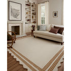 A large cream-colored area rug with a scalloped border and tan stripe accents, styled in a bright, modern living room with a cream sofa, fireplace, and built-in shelves.