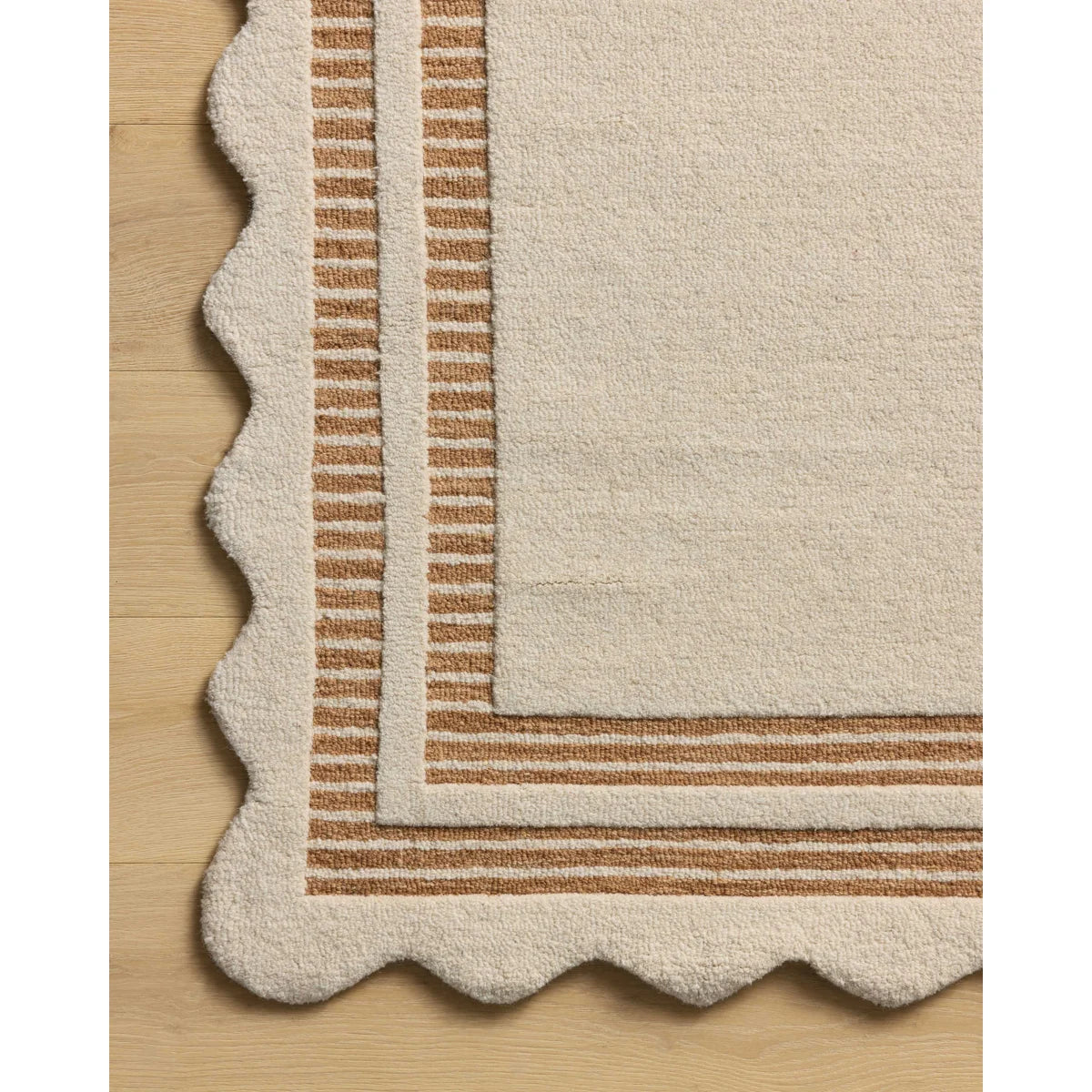 Close-up of a cream-colored area rug with a scalloped edge and striped border, shown on a light wood floor.