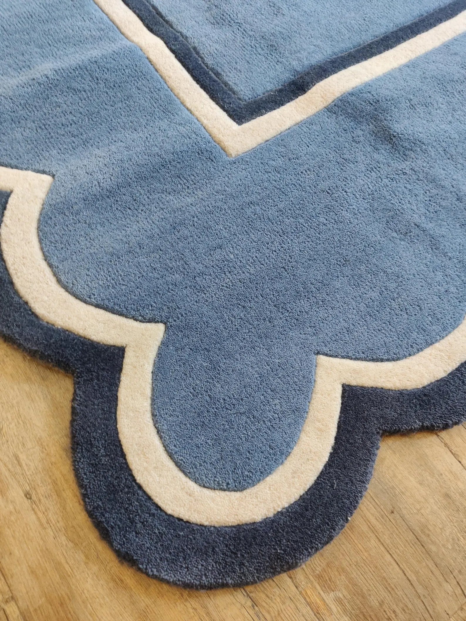 A close-up of a blue patterned area rug with scalloped edges and cream borders, shown on a light wood floor.