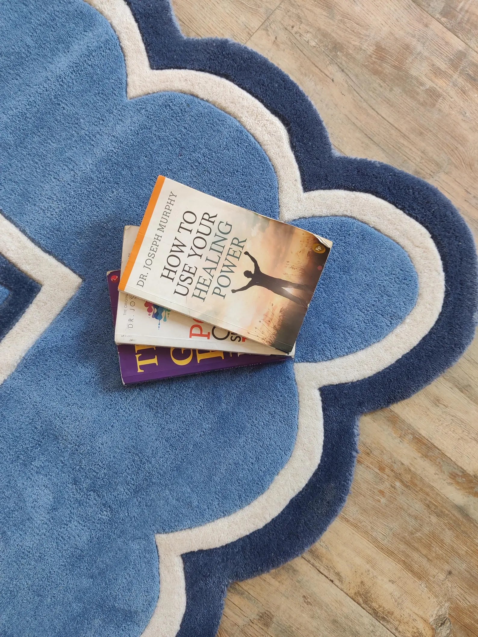 A stack of two books, with the top book titled 'How to Use Your Healing Power' by Dr. Jennifer Muehle, placed on a blue and white cloud-shaped rug over a light wood floor.