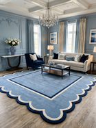 A large scalloped area rug in light blue with navy and cream borders, shown in a styled living room with a sofa, armchair, coffee table, and blue walls.