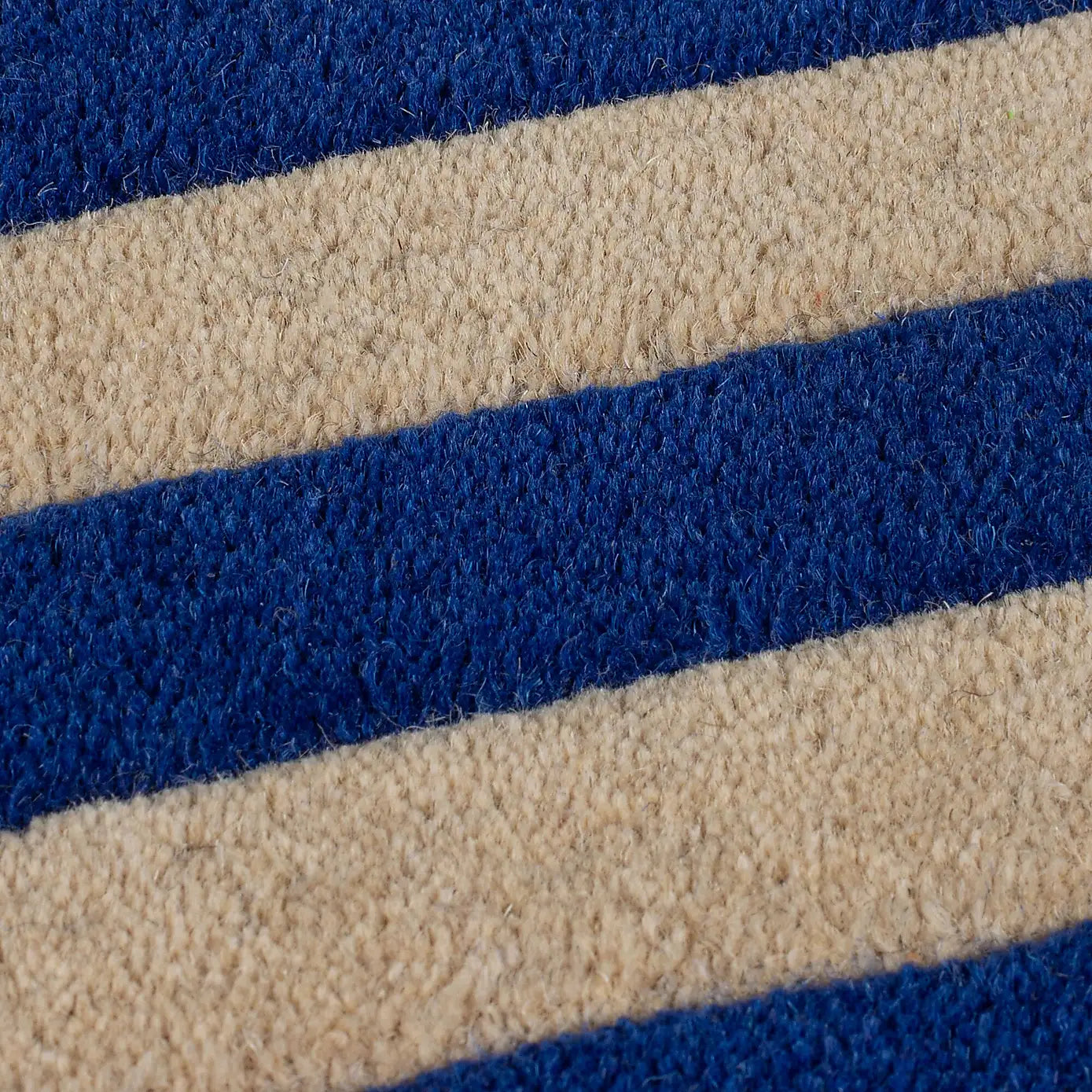 A close-up of a textured rug with alternating horizontal stripes of deep blue and warm beige.