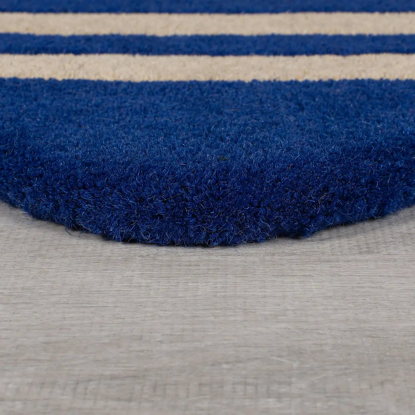 A close-up of a plush, high-pile shag rug with bold horizontal stripes in royal blue and cream, shown resting on a light gray textured floor.