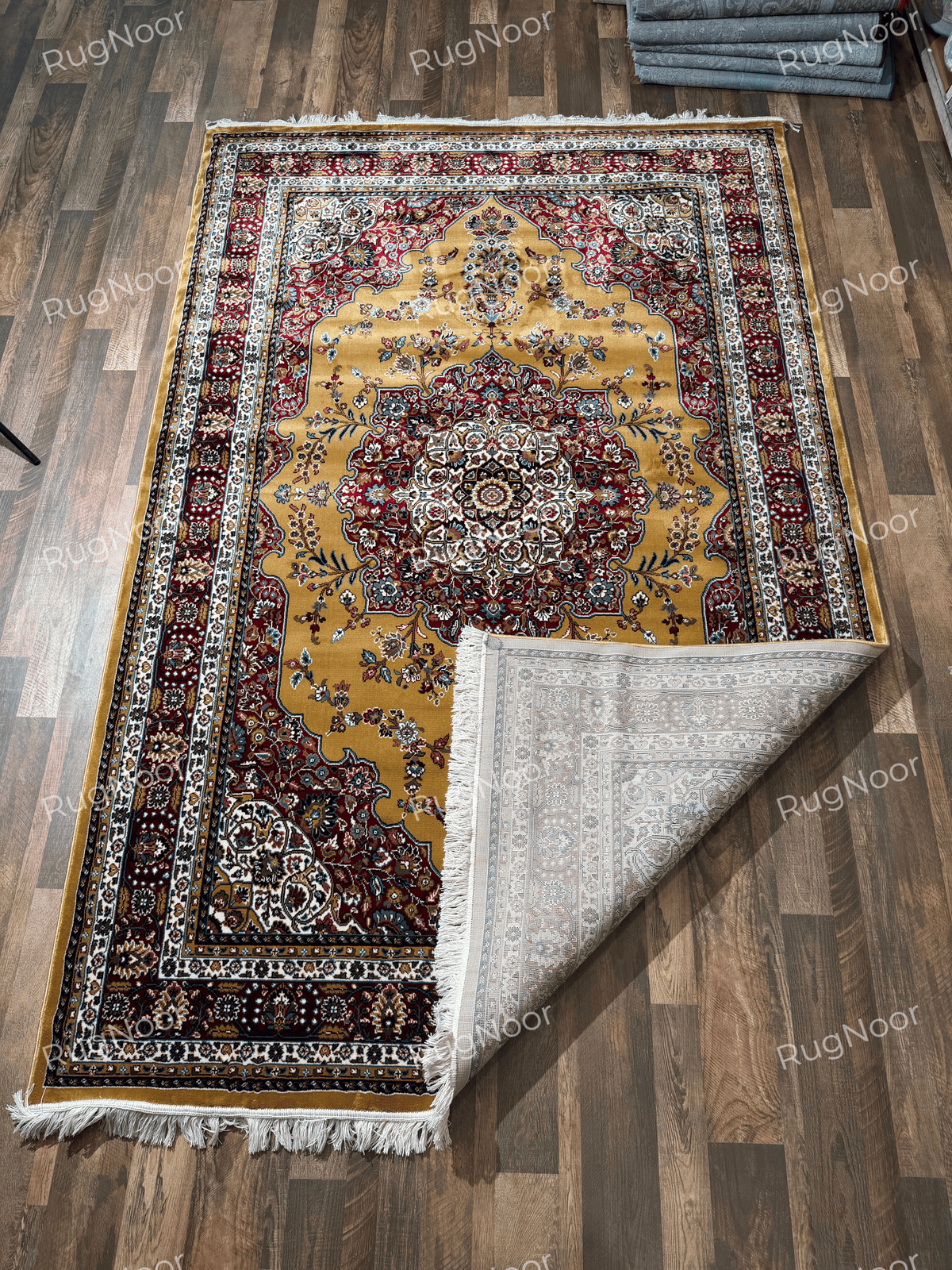 Full view of mustard gold traditional rug with central medallion and folded corner showing backing - Shams RugNoor