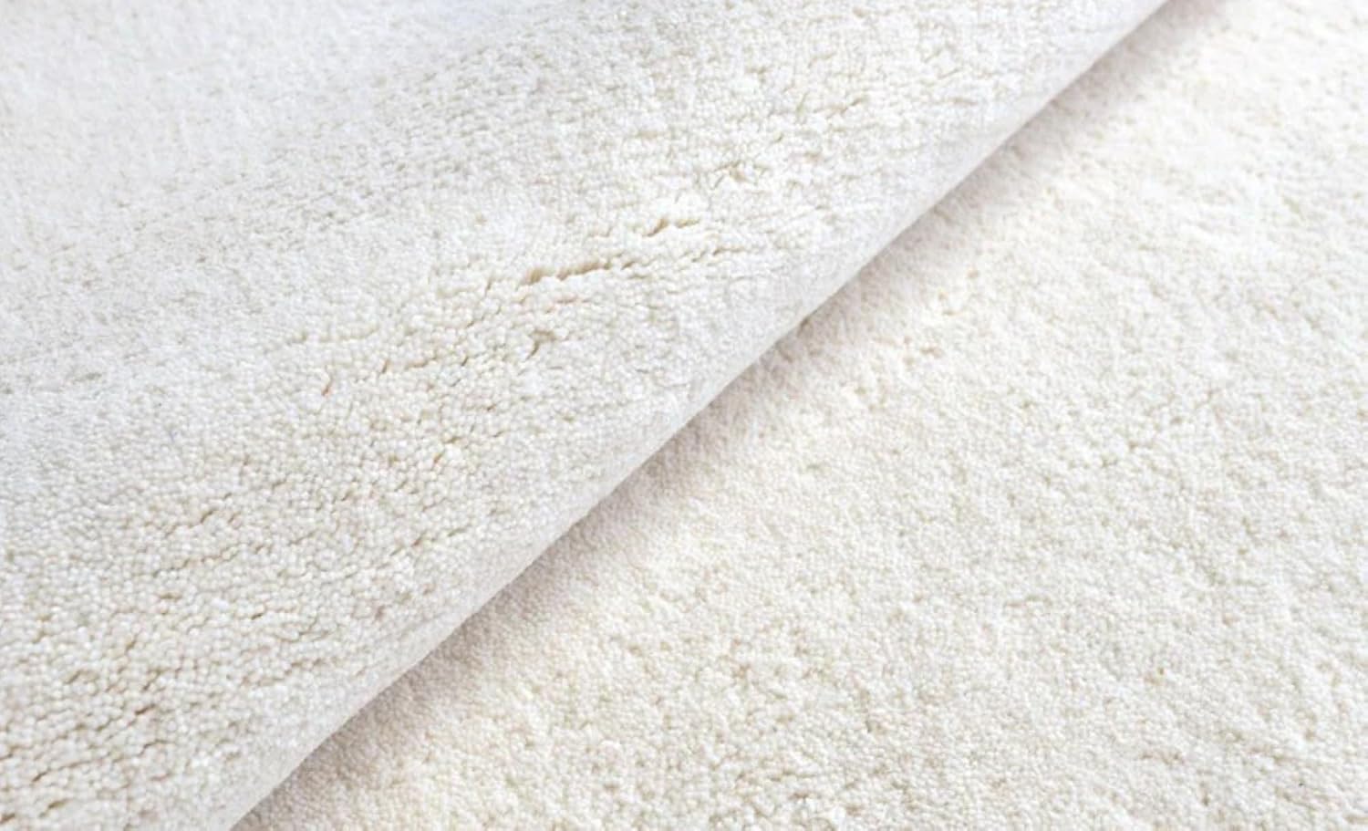 Hand-tufted white wool rug edge detail showing plush pile and finished binding