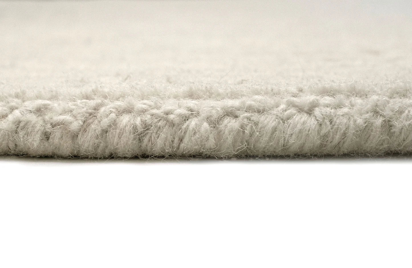 Close-up of a plush, high-pile rug in a light cream or off-white color, showing the thick, textured pile and the tuck edge against a white background.