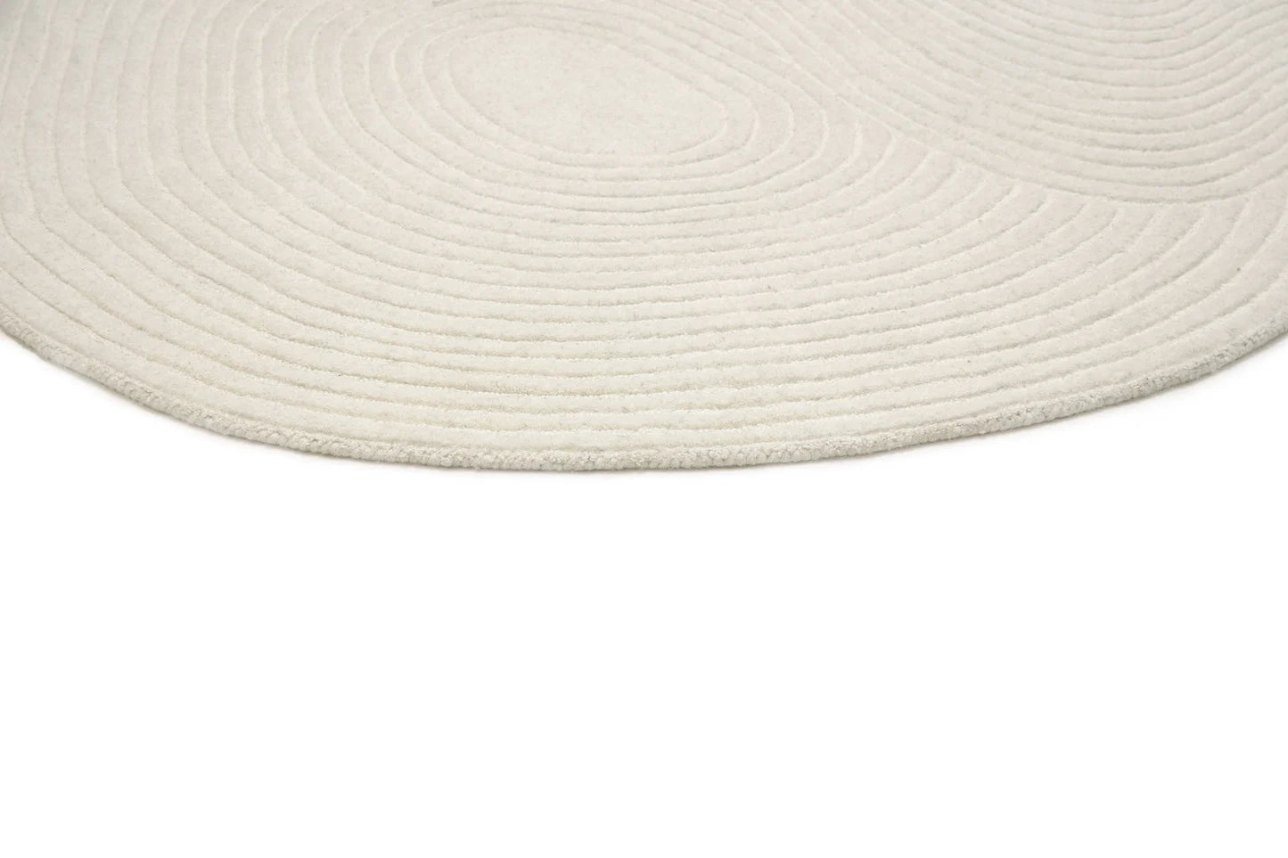 A close-up of a round woven rug in a warm off-white or cream color, showing the concentric circular texture of the braided fibers against a plain white background.