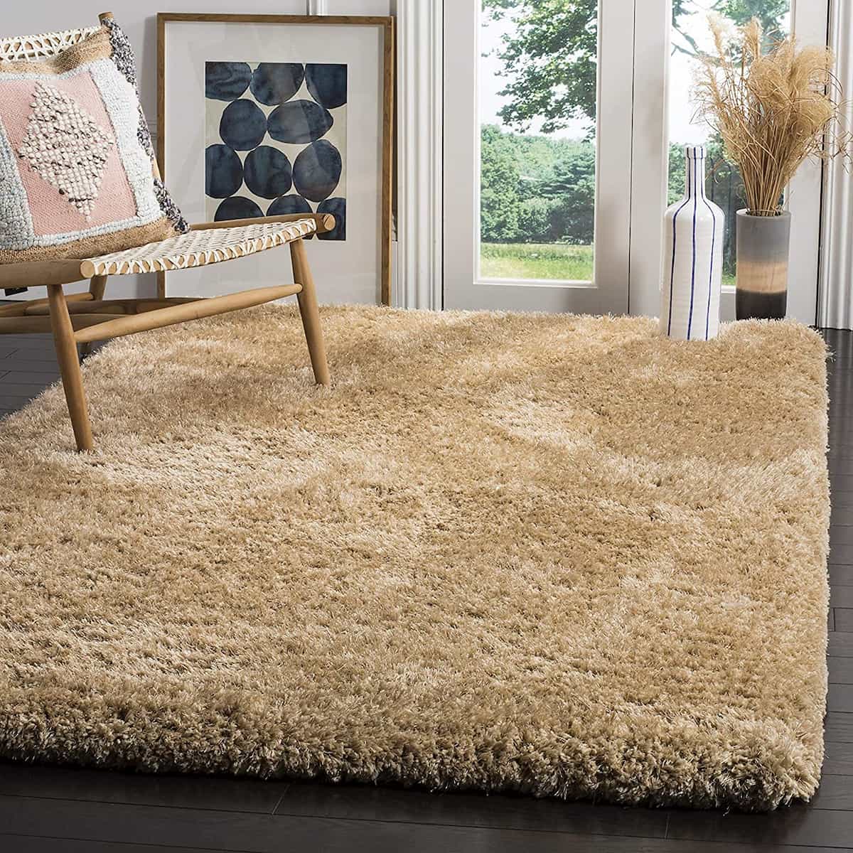 A beige solid microfiber and silk shaggy rug placed on a floor in a room with a chair and a framed picture - RugNoor