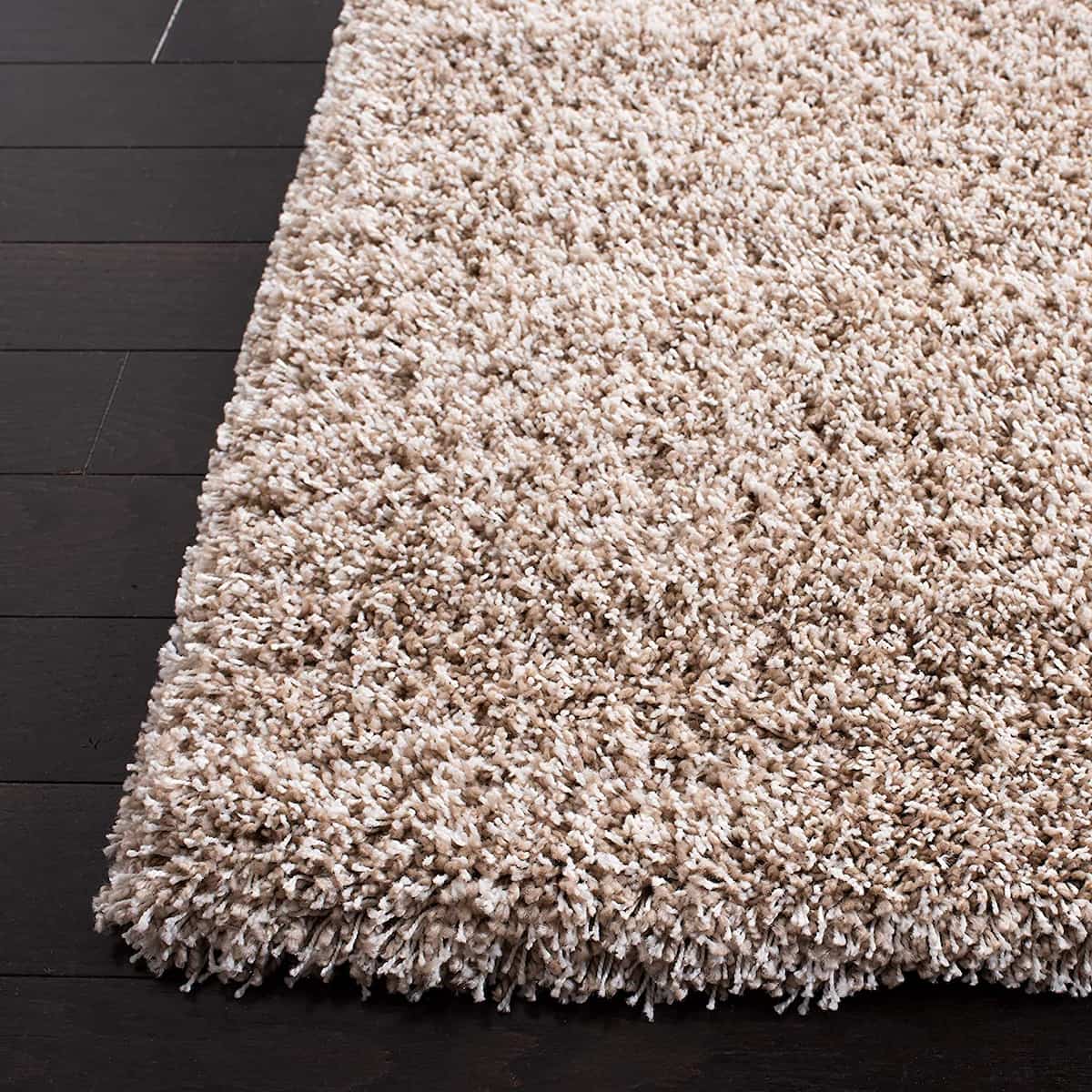 Close-up of thick beige shaggy rug pile edge on wooden floor - RugNoor