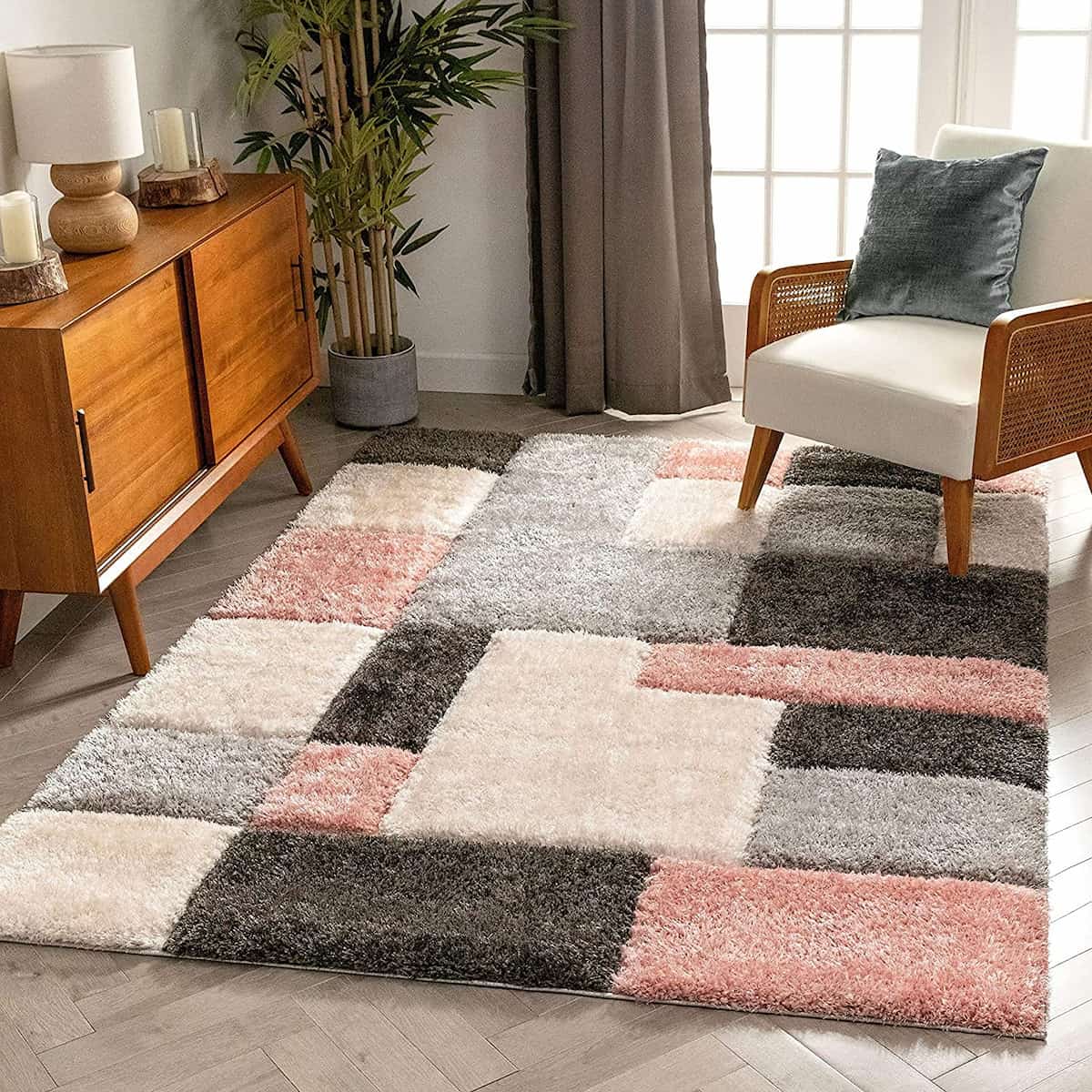 A RugNoor's shaggy rug with a geometric pattern in pink, grey, black, and white colors, placed on a floor in a room with furniture.