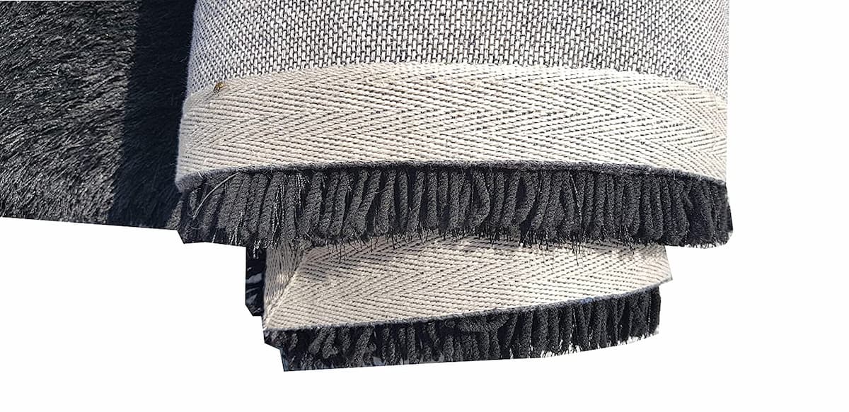 Rolled edge of black shag rug showing binding stitching - RugNoor