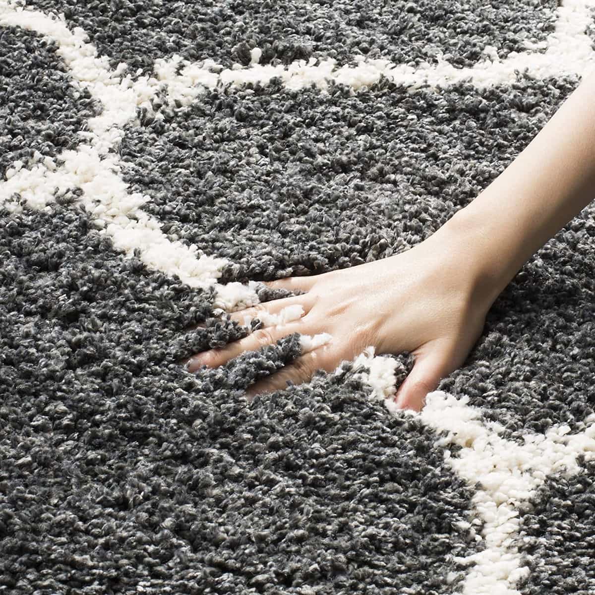 Charcoal grey and ivory Moroccan trellis shaggy rug – soft texture close-up with hand, RugNoor