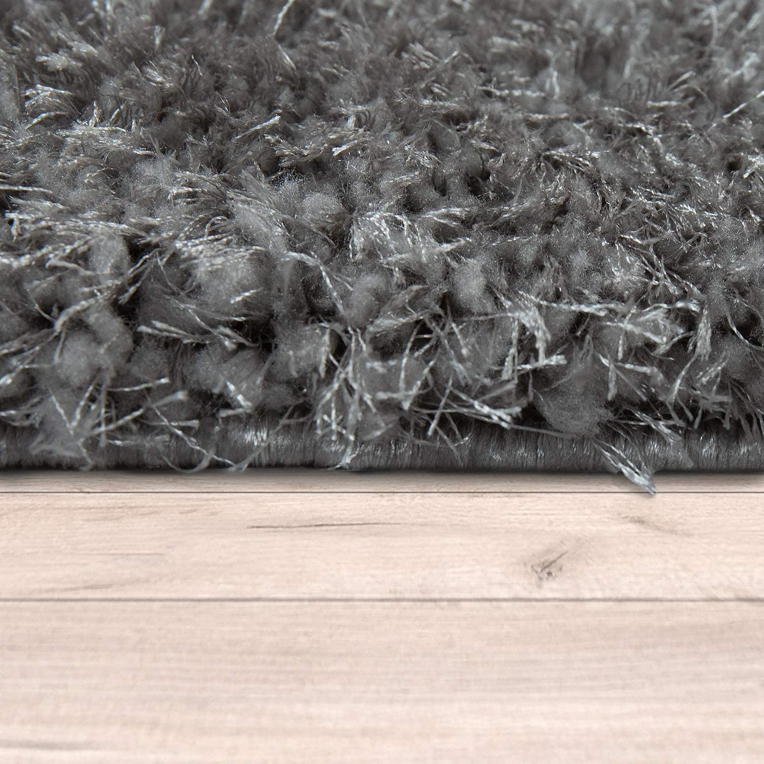 Dense dark grey rug fibers photographed at floor level on hardwood