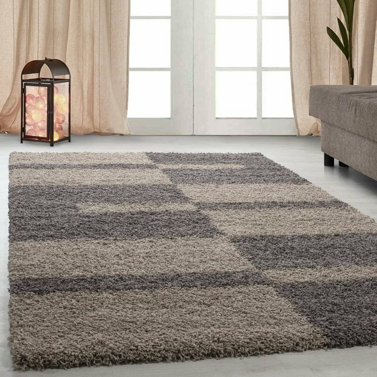 RugNoor shaggy rug with a block pattern in brown colors, placed on a floor in a room with a window and a lamp.