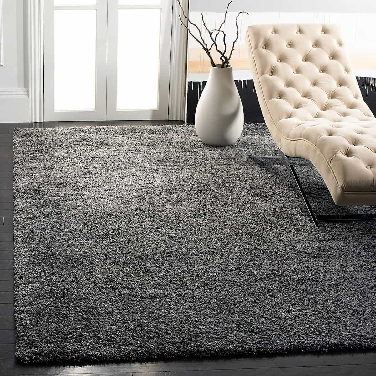 A dark grey fluffy shaggy rug in a living room setting with a white vase on top and a white chair in the background.