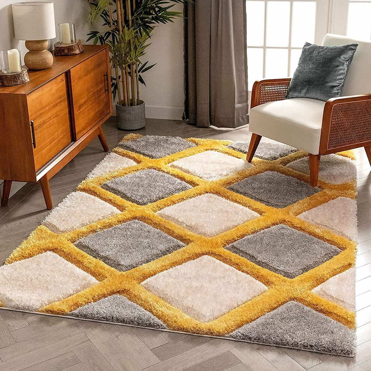 A RugNoor's grey and yellow diamond-shaped design microfiber and silk shaggy rug on a floor, with a chair and wooden cabinet in the background.