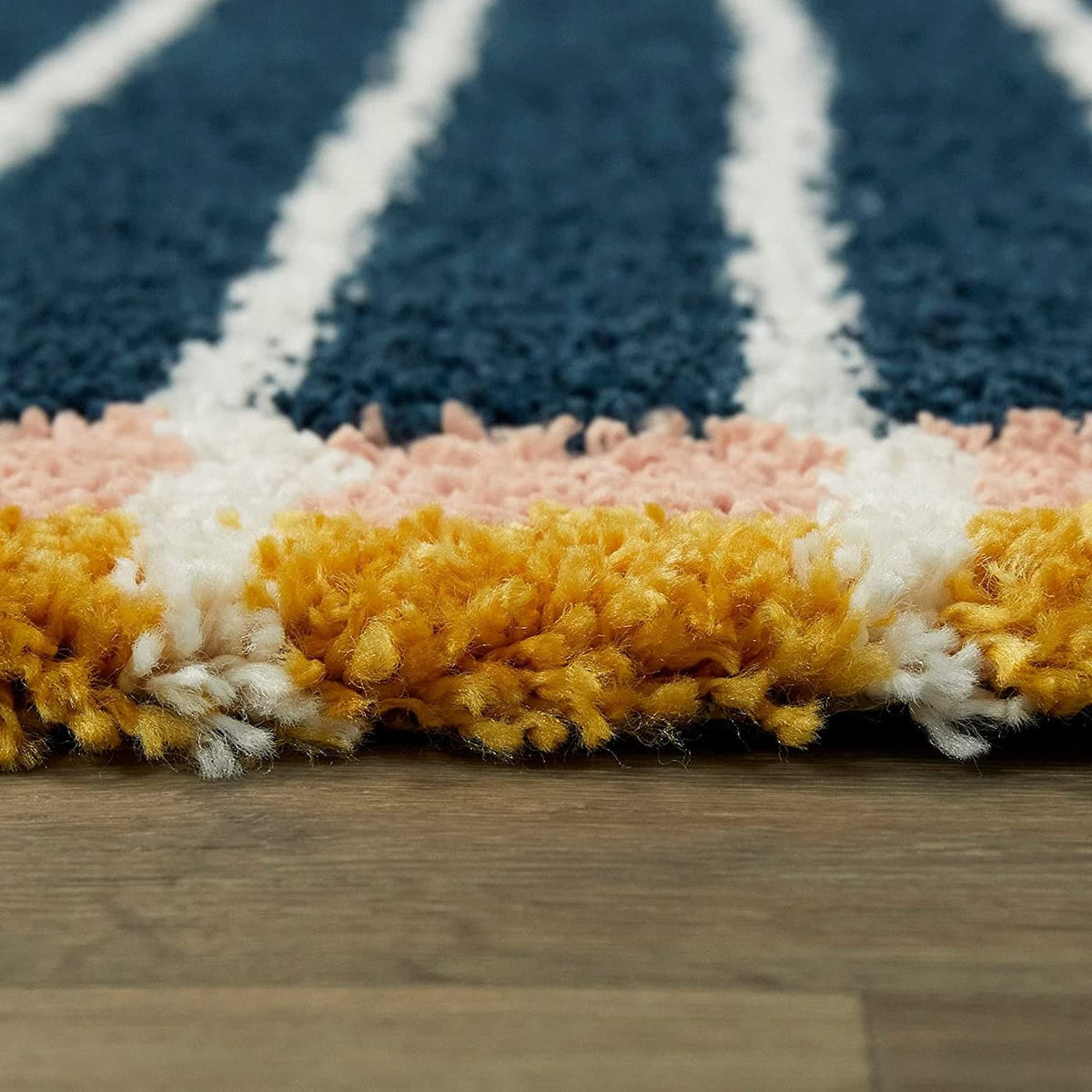 Ground-level view of navy white striped shag rug edge with pink yellow border, RugNoor fluffy carpet