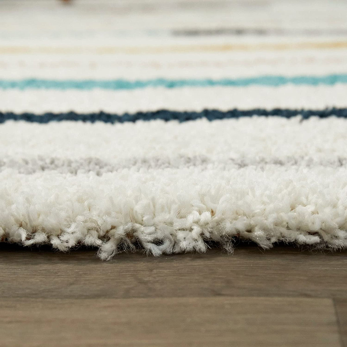 Ground-level close-up of white shag rug edge with blue, navy stripes, RugNoor fluffy carpet