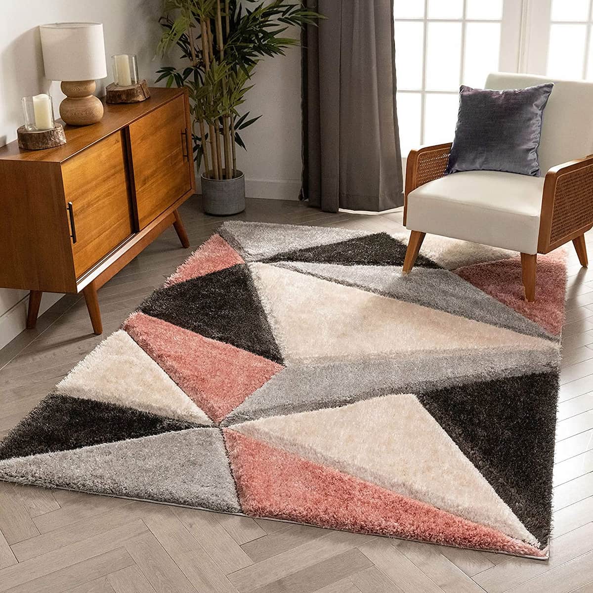 A RugNoor's diamond-shaped, shaggy rug with a pattern of pink, cream, grey, and black colors, placed on a floor in a room with furniture.