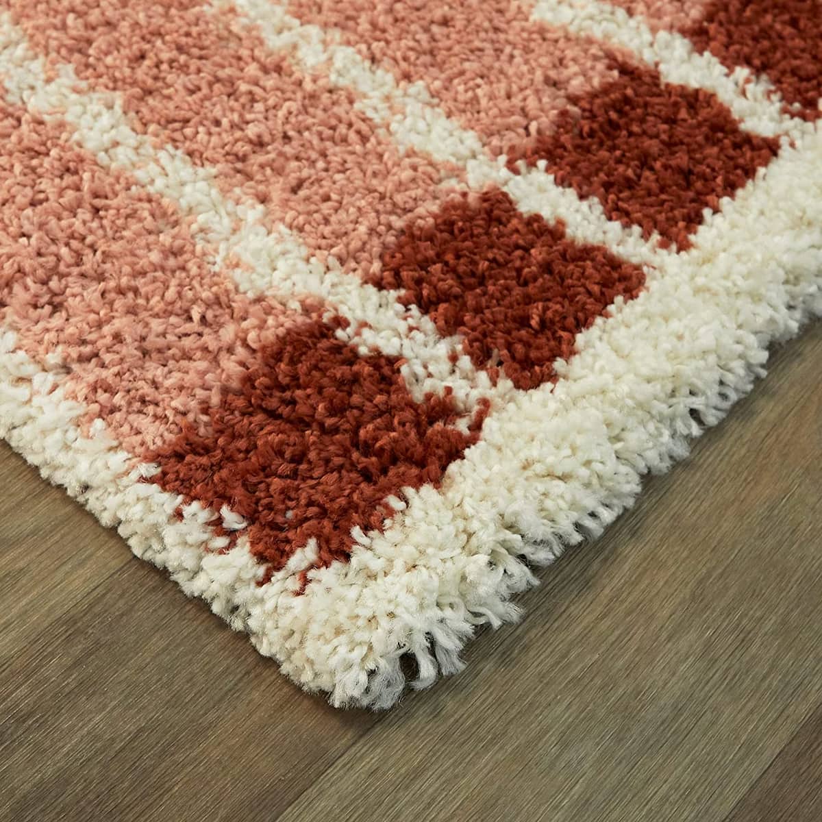 Corner close-up of pink rust checkered shag rug pile texture, RugNoor soft carpet on wood floor