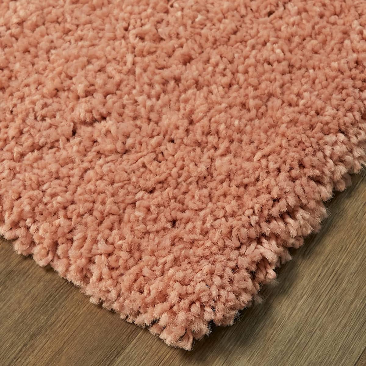 RugNoor corner close-up pink shag rug pile texture, soft fluffy carpet on wooden floor
