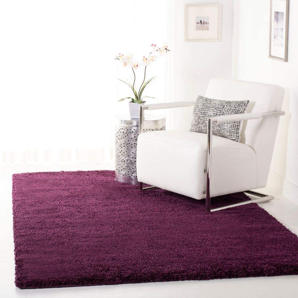 A purple microfiber shaggy rug in a living room setting with a white armchair and a small table with a plant on it in the background - RugNoor