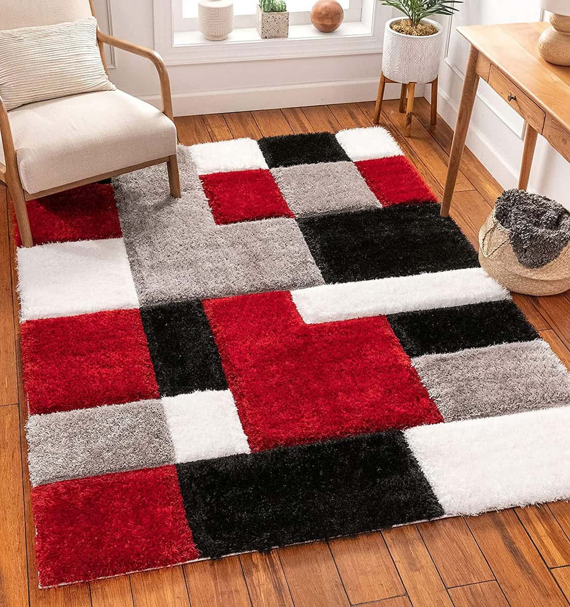 A RugNoor's shaggy rug with a geometric pattern of red, black, and white blocks placed on a wooden floor, with furniture around it.