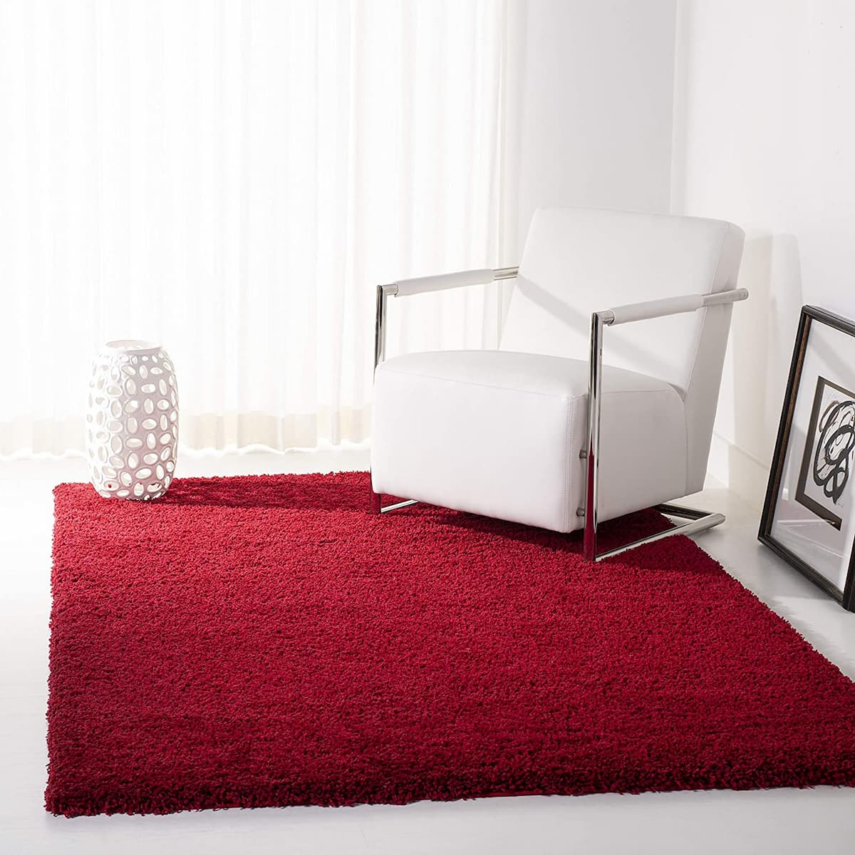 A red microfiber shaggy rug placed on the floor under a white armchair in a room with a light source creating a glare on the rug - RugNoor