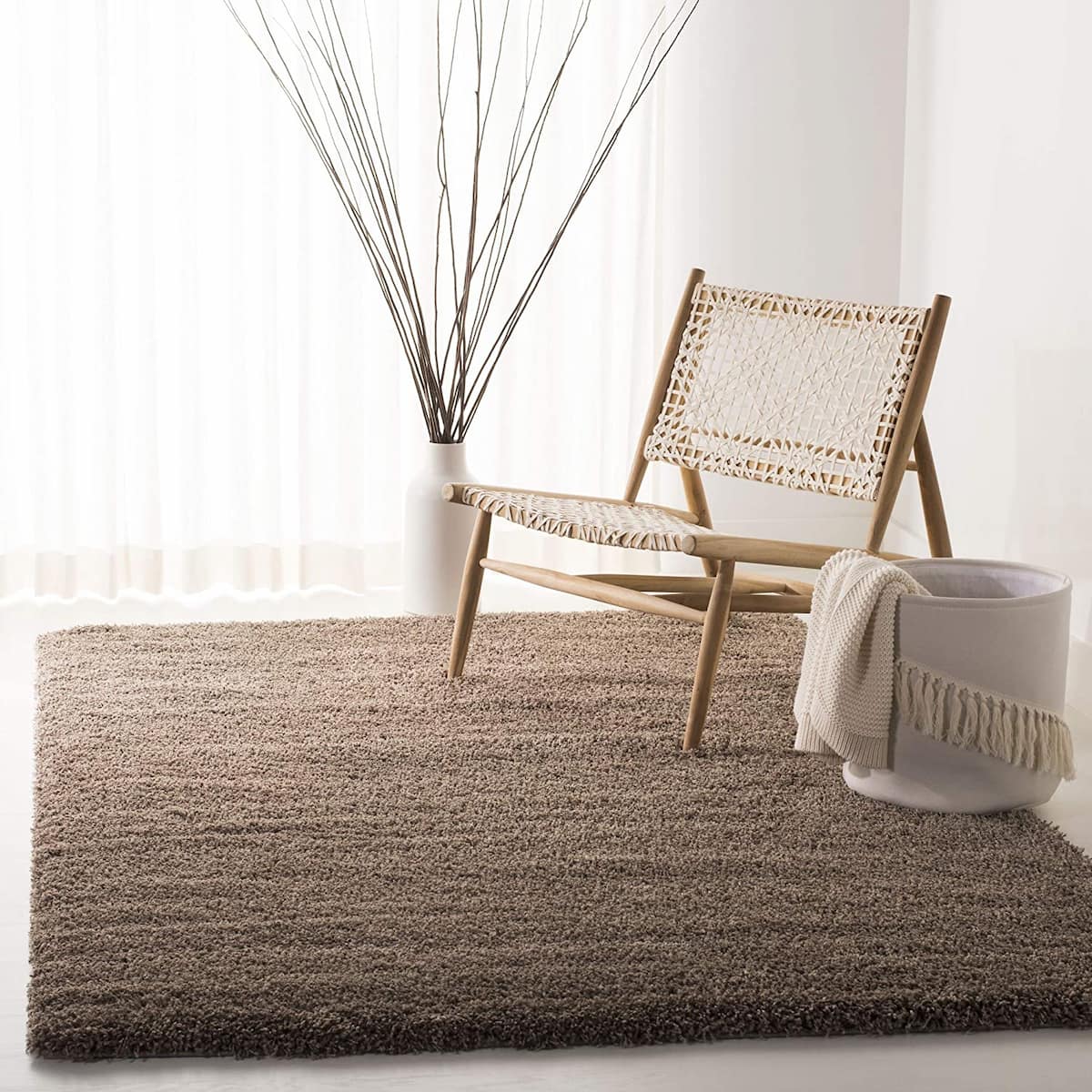 A taupe solid microfiber shaggy rug placed on the floor, with a chair and a plant in the background and a white vase in the foreground - RugNoor