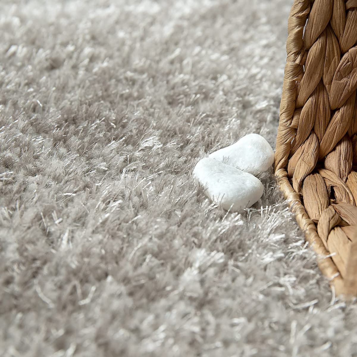 Close-up of RugNoor's soft grey shaggy carpet pile styled with stones and rattan texture