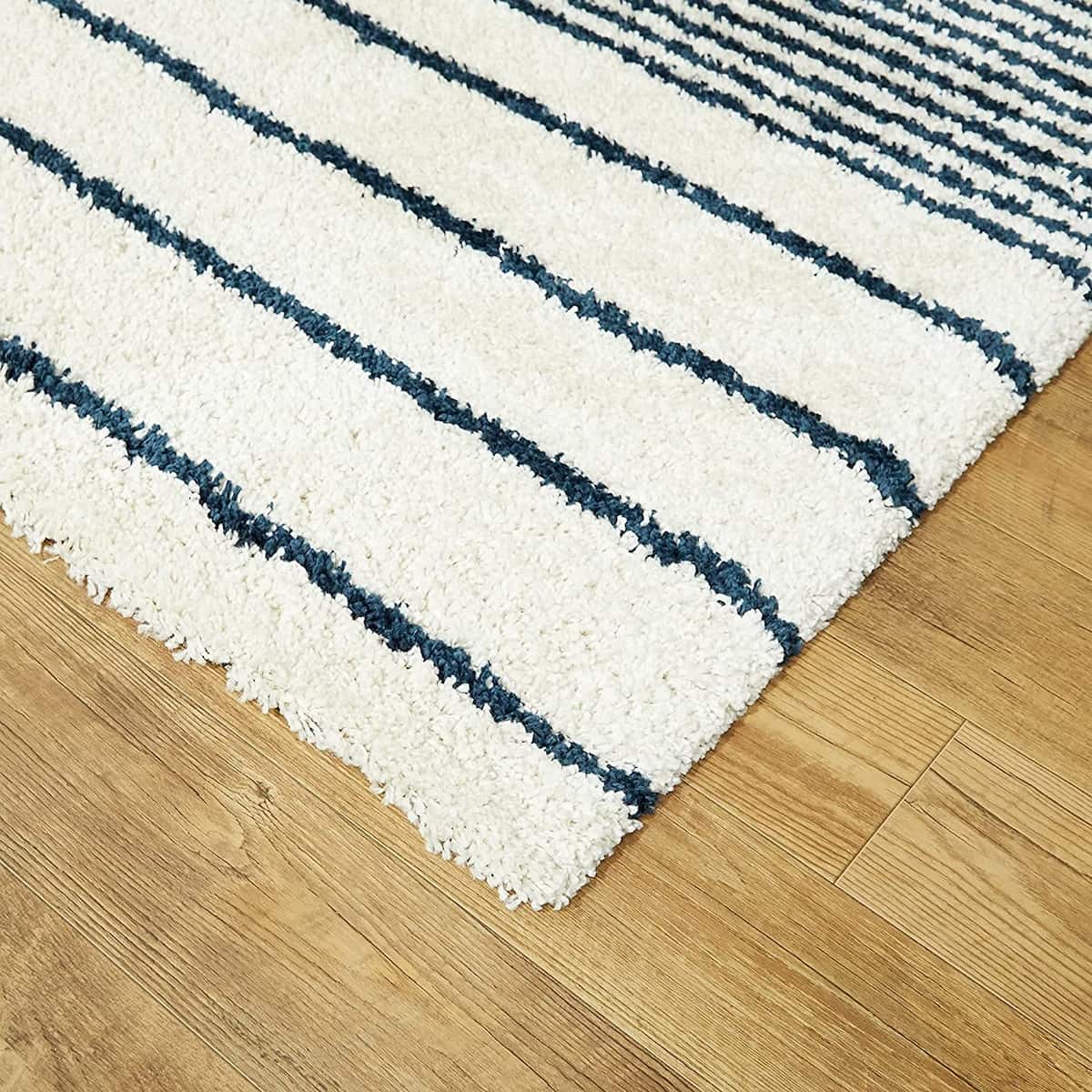Corner close-up of white shaggy rug pile with navy pinstripes, RugNoor soft-touch carpet on wood floor
