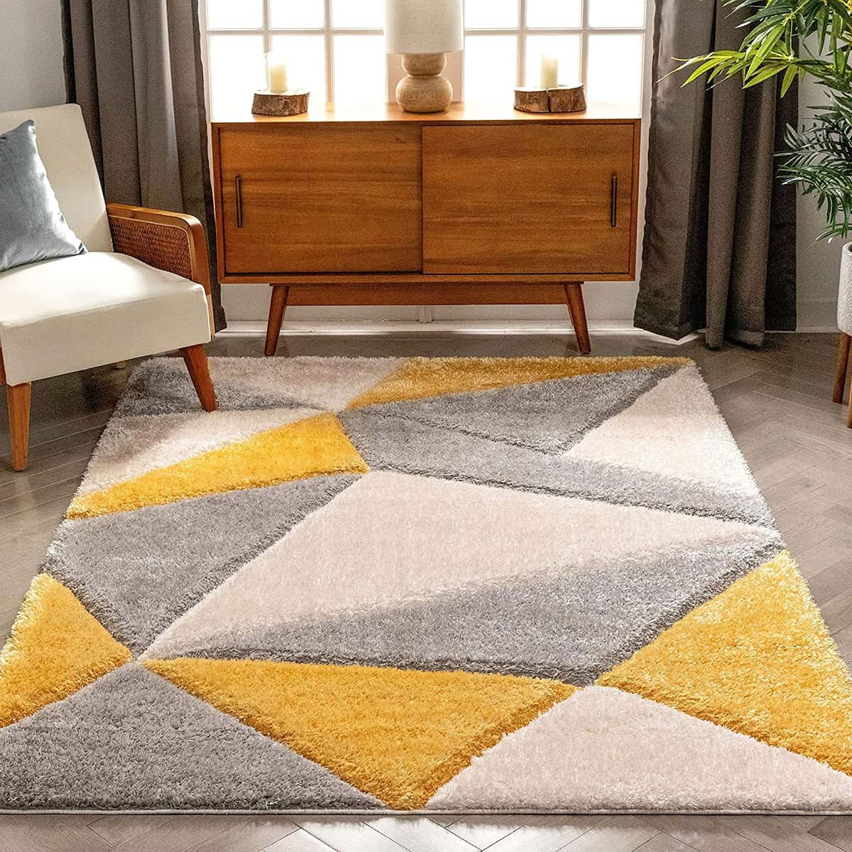A RugNoor's shaggy rug with geometric diamond patterns in gray, white, and yellow, placed on a floor in a room with a wooden cabinet and a chair.